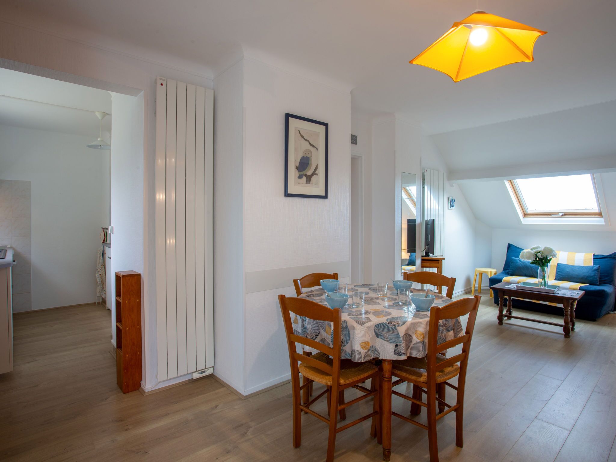 Un comedor con una mesa preparada para cuatro personas, sillas de madera y una lámpara colgante amarilla.