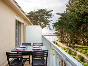 A balcony with a table set for two, overlooking a body of water and a forested area.
