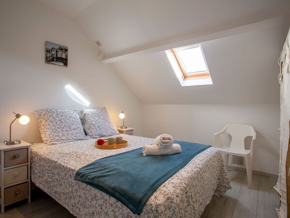 A bedroom with a skylight, a bed with floral bedding, a bedside table with a lamp, and a white chair.