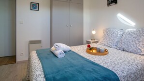 Un dormitorio con cama, armario, mesita de noche con lámpara y un cuadro pequeño en la pared.