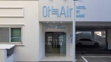 La entrada al hotel Ot=Air by AANK, con un diseño moderno y fachada de vidrio, además de un estacionamiento visible.