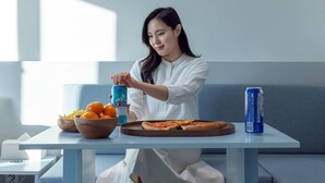 Une personne est assise à une table devant un bol d’oranges, une pizza et une canette de boisson.