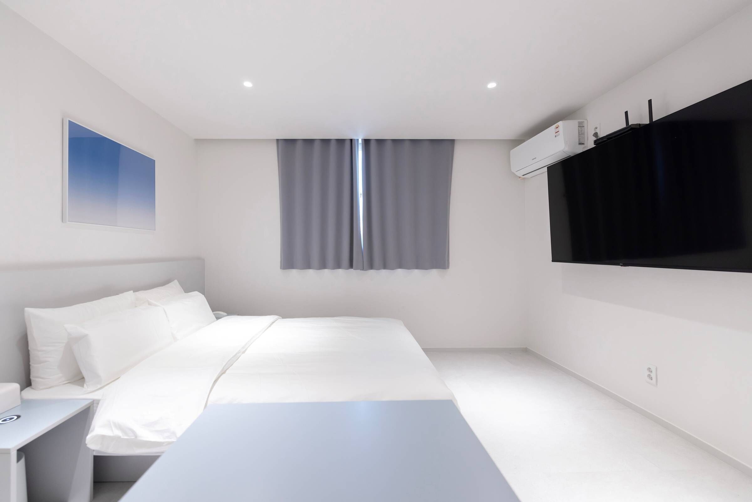 Una habitación de hotel moderna con cama, mesita de noche y televisión de pantalla plana.