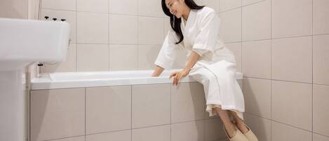 Una persona sentada al borde de una bañera en un baño con paredes y piso de azulejos.