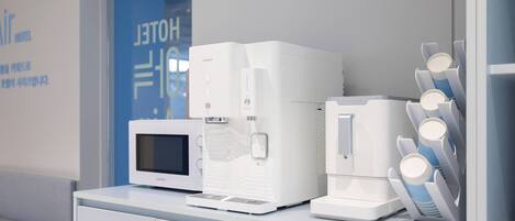 Un área de kitchenette con microondas, cafetera y dispensador de toallas de papel.