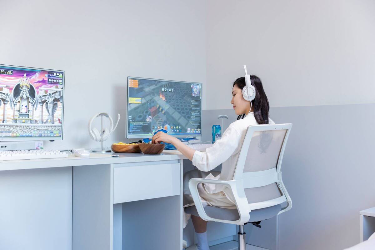 Une personne assise à un bureau, devant deux écrans, un clavier et une souris.