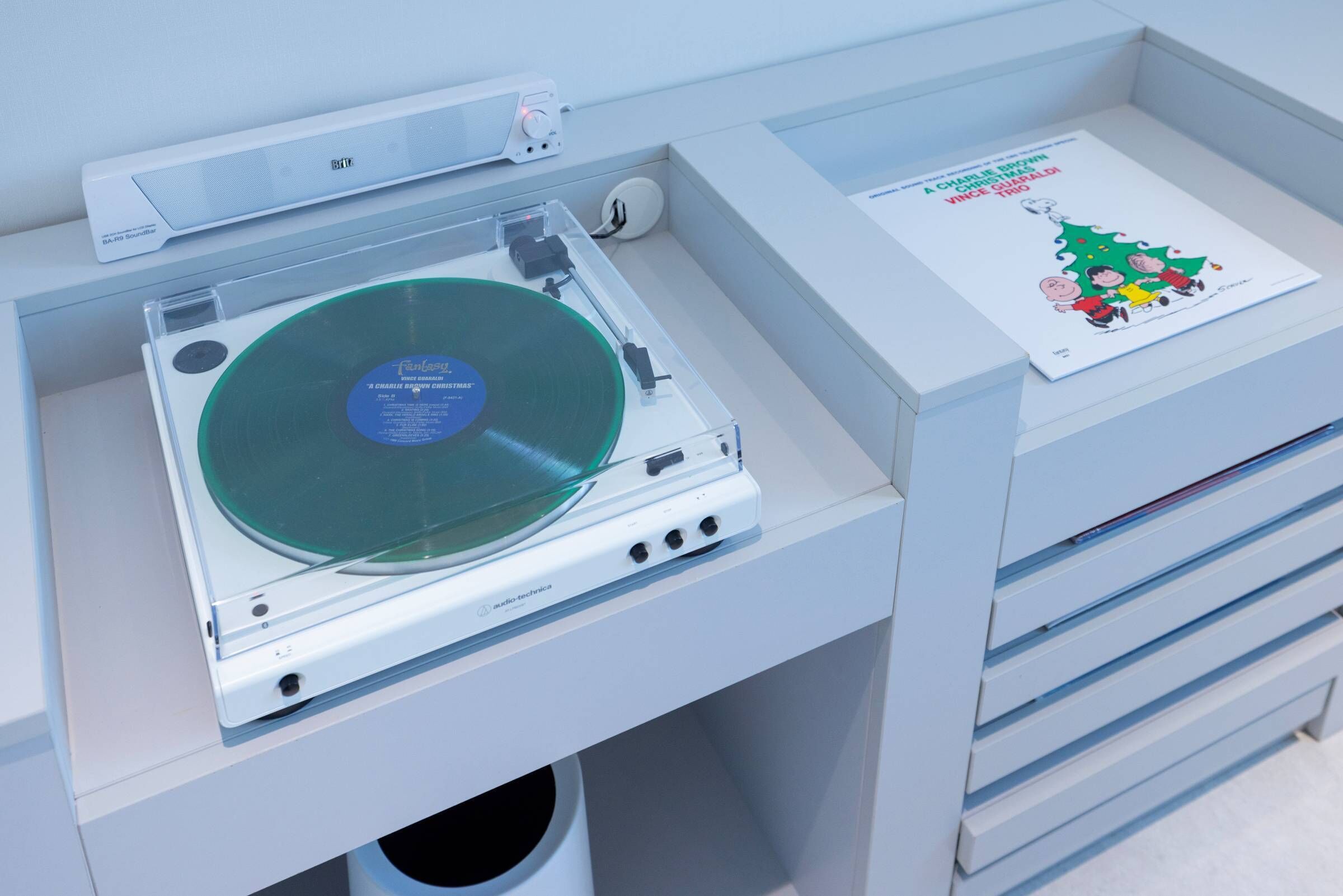 Une platine vinyle avec un disque, une imprimante et un tableau représentant un sapin de Noël, le tout posé sur un bureau.