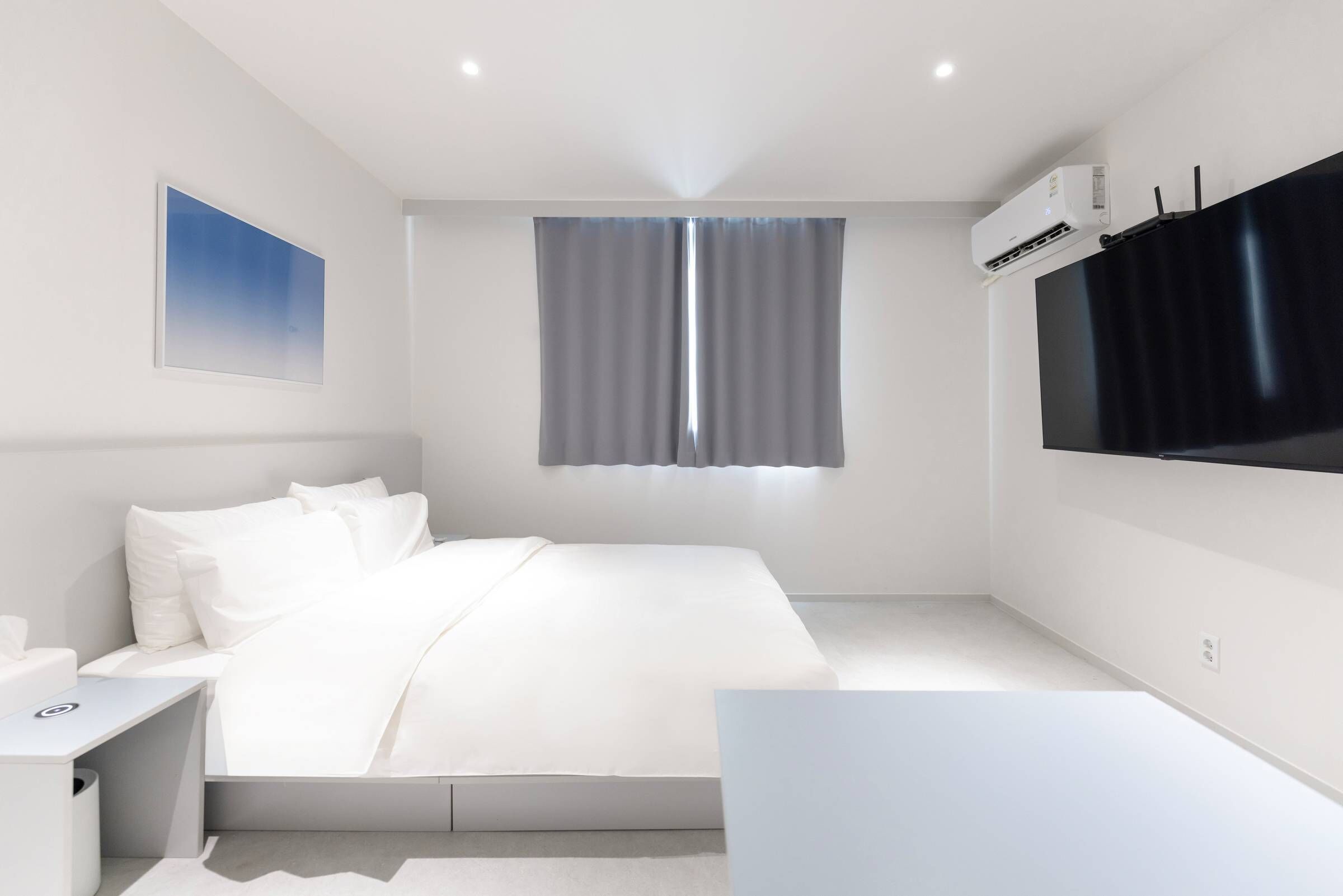 Ein modernes Hotelzimmer mit Bett, Nachttisch und einem großen, an der Wand befestigten Flachbildfernseher.