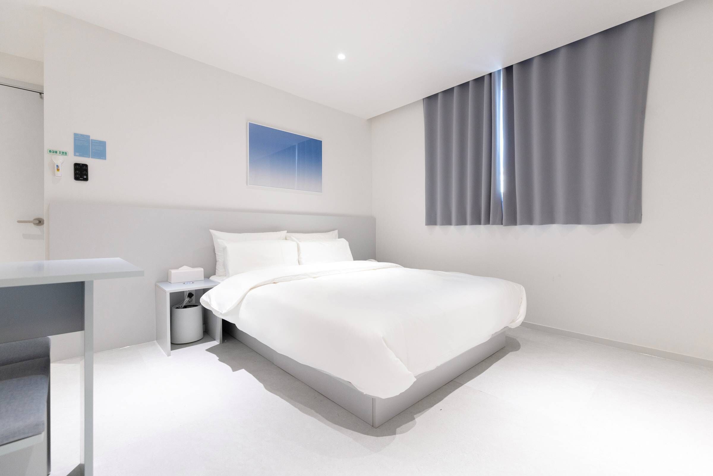 Una habitación de hotel moderna con una cama grande, una mesita de noche, un escritorio pequeño y una ventana con cortinas.