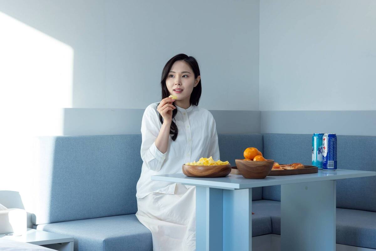 Une personne est assise à une table devant un bol de nourriture, une assiette d’oranges et deux canettes de bière.