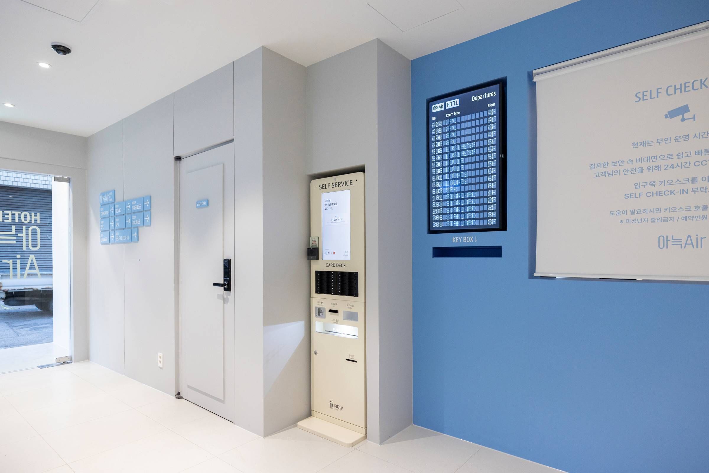 A modern hotel lobby with a self-service card deck, a digital departure board, and a self-check-in kiosk.