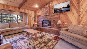 A cozy cabin interior with a fireplace, wooden walls, and a large window.