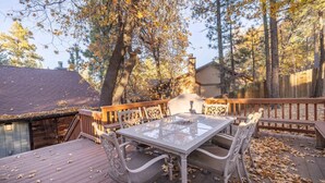 A deck with a glass-top table and chairs, surrounded by trees and a wooden fence.