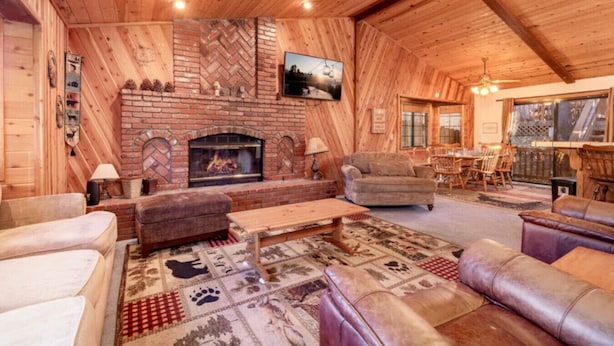 A cozy log cabin interior with a fireplace, leather sofas, and a dining area.