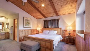 A wooden-framed bedroom with a bed, bedside lamps, a nightstand, a bench, and a painting on the wall.