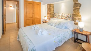 A bedroom with a bed, a wooden wardrobe, a stone accent wall, and a nightstand with a lamp. - Can Verdal by Interhome (Sant Miquel de Balasant)