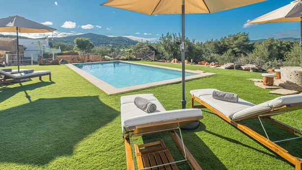 A poolside area with a rectangular pool, two lounge chairs, and a large umbrella. - Can Verdal by Interhome (Sant Miquel de Balasant)