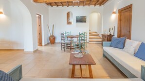 A spacious living area with a wooden ceiling, a sofa, a coffee table, and a dining table with chairs. - Can Verdal by Interhome (Sant Miquel de Balasant)