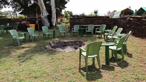 An outdoor seating area with green plastic chairs and tables, a fire pit, and a rustic stone wall in the background. - Baraka Camp (Isiolo)