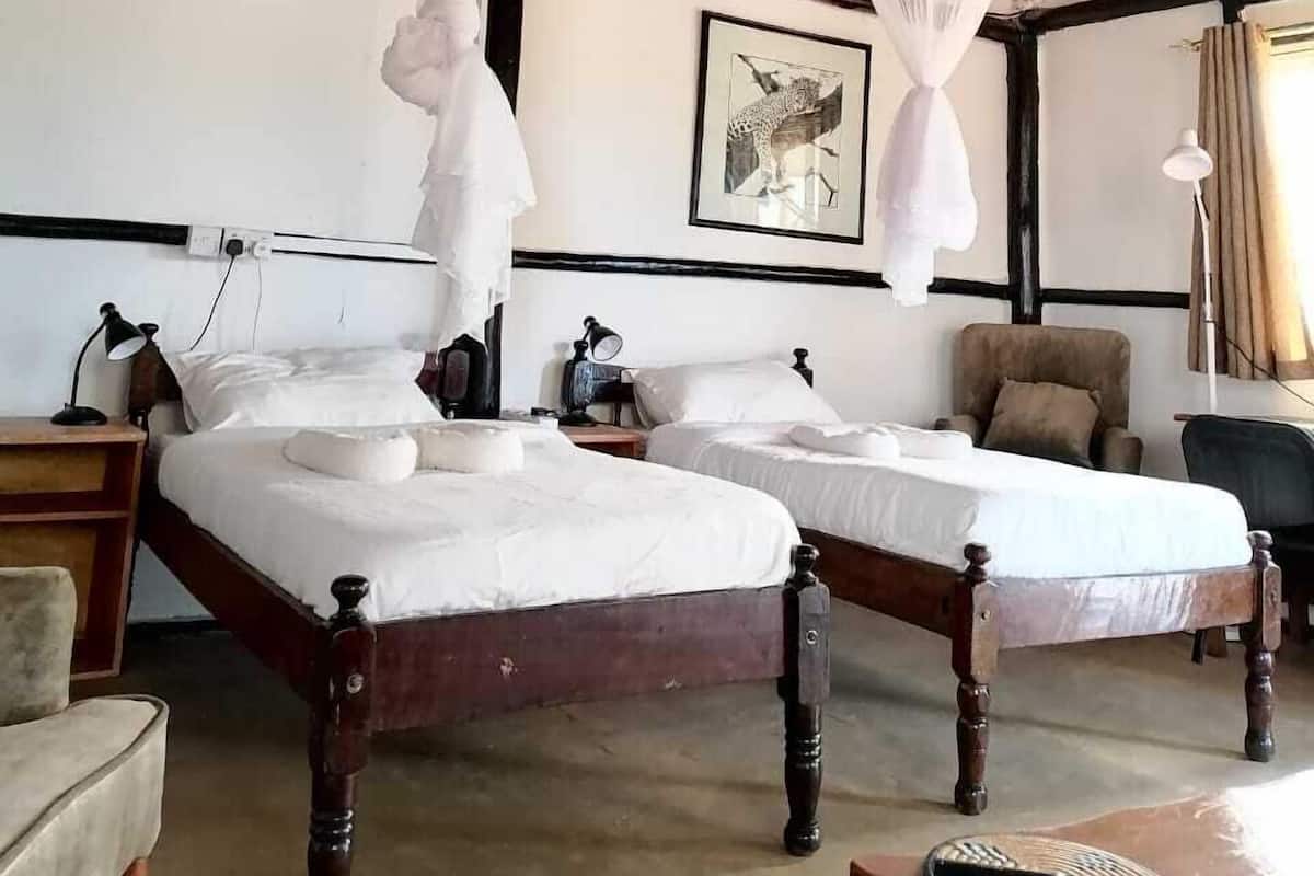 A room with two beds, a chair, a table, and a ceiling with wooden beams.