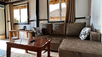 Una habitación con techo de paja, un sofá, una mesa de madera y una ventana con cortinas.