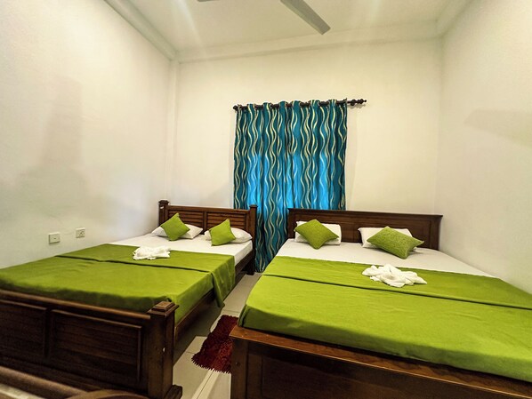 Una habitación con dos camas individuales, cada una con colcha y almohadas verdes, cabeceros de madera y una cortina azul.