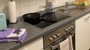 Una cocina con estufa, microondas y horno. Hay un lavaplatos con un escurreplatos y una tabla de cortar de madera.