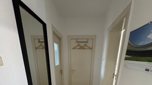 Un pasillo estrecho con suelo de madera, paredes blancas y un espejo grande a la izquierda.
