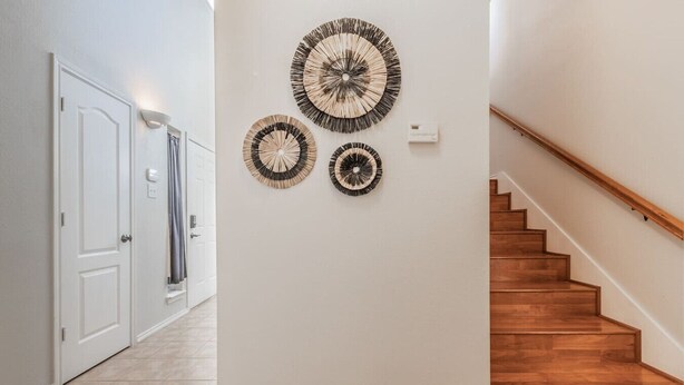A hallway with a wooden staircase, white walls, and three wall-mounted circular wall art pieces. - Cozy Vibe in Frisco/Little Elm (Little Elm)