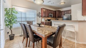 A modern kitchen with dark wooden cabinets, a granite countertop, and a dining area with a marble table and leather chairs. - Cozy Vibe in Frisco/Little Elm (Little Elm)