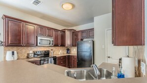 A kitchen with dark wooden cabinets, a stainless steel refrigerator, a microwave, an oven, a sink, and a countertop. - Cozy Vibe in Frisco/Little Elm (Little Elm)