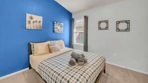 Une chambre avec un mur d’accent bleu, un lit recouvert d’une courtepointe à carreaux et deux œuvres d’art murales.