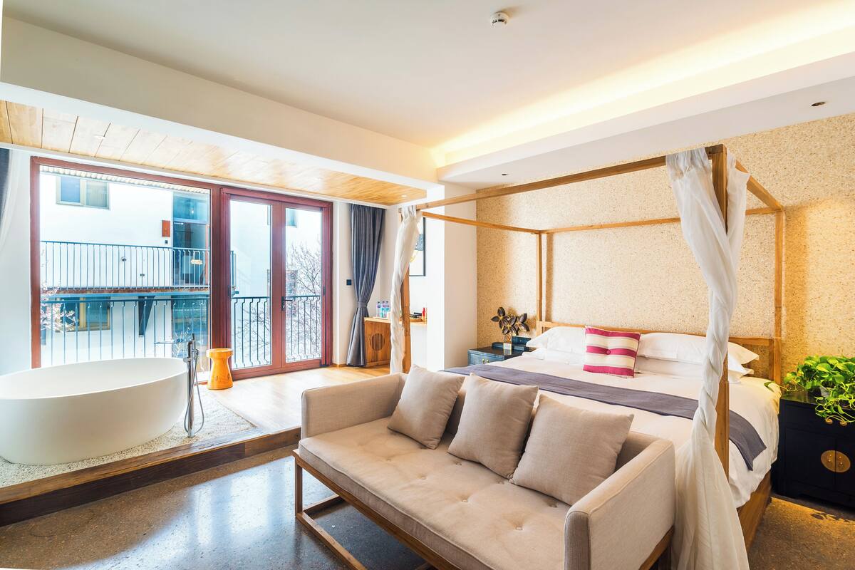 A modern bedroom with a large bed, a sitting area, and a bathtub.