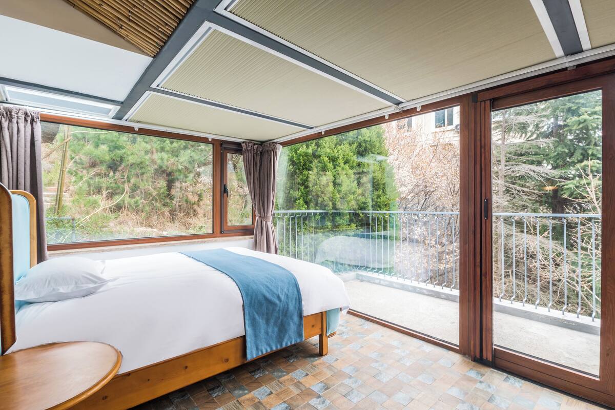 A bedroom with a large bed, a wooden nightstand, and a view of a balcony with a railing.