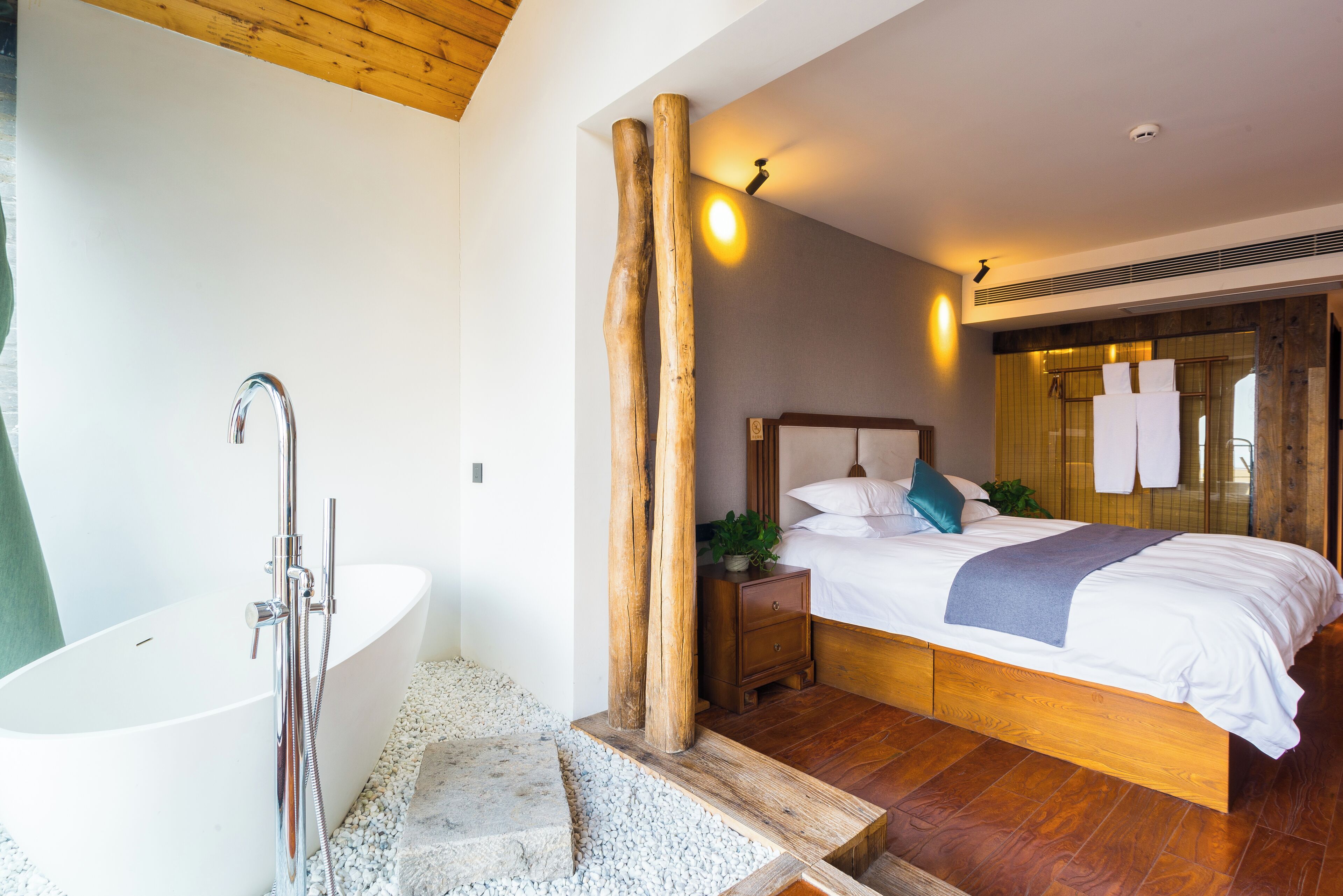 Un dormitorio moderno con una cama grande, una mesita de noche de madera, una bañera blanca y un techo de madera.