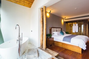 A modern bedroom with a large bed, a wooden nightstand, a white bathtub, and a wooden ceiling.