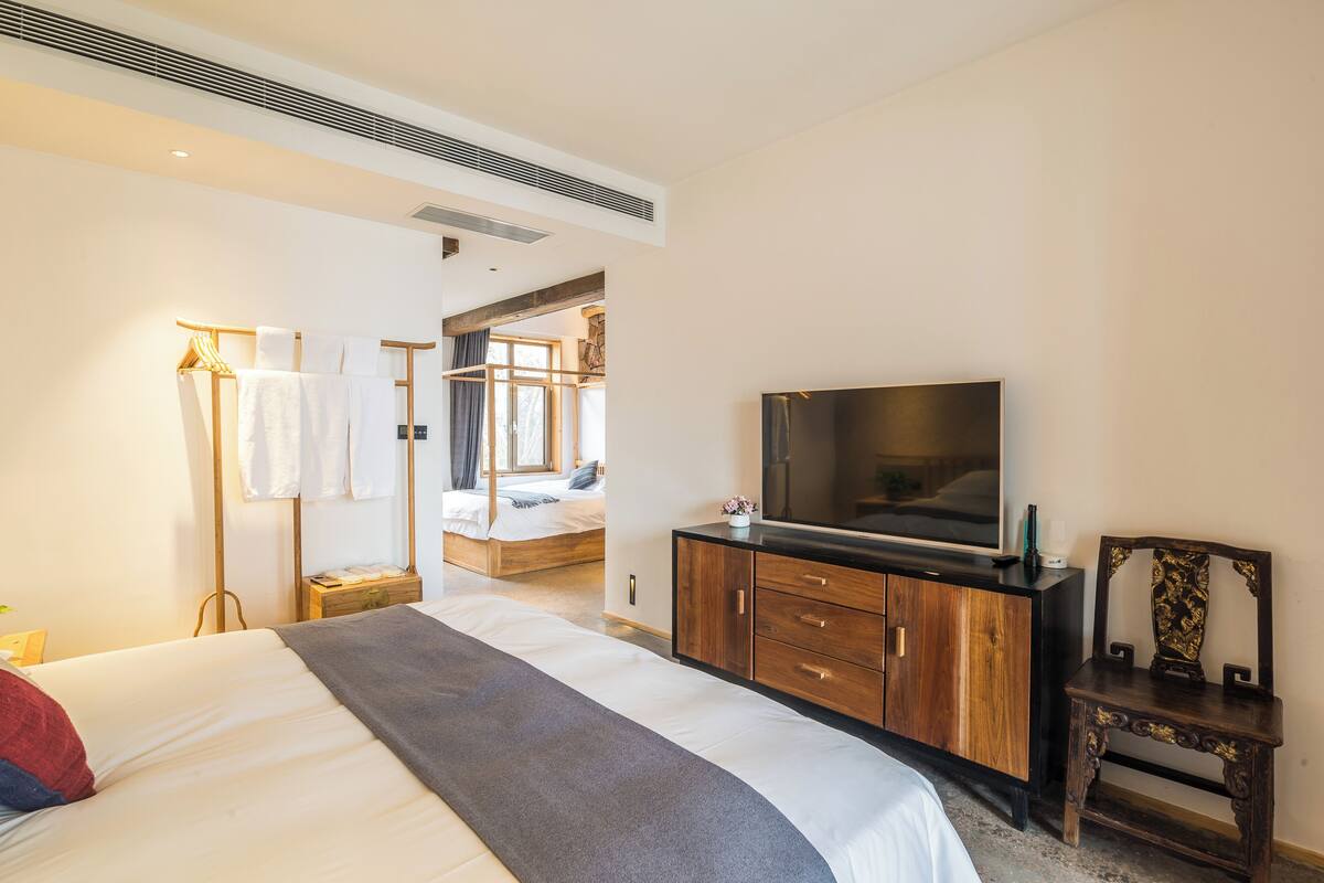 A modern hotel room with a large bed, a flat-screen TV, a wooden dresser, and a walk-in closet.