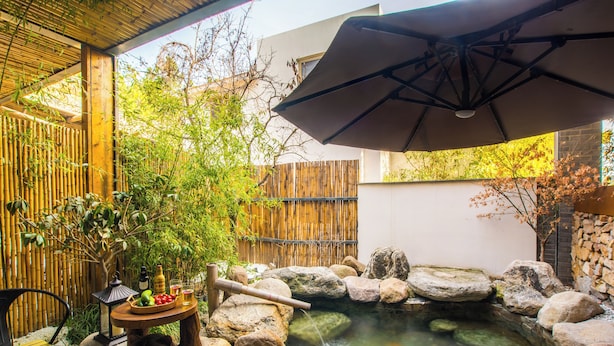 Un jardín tranquilo con estanque de carpas, cerca de bambú y una mesa con bebidas y aperitivos.