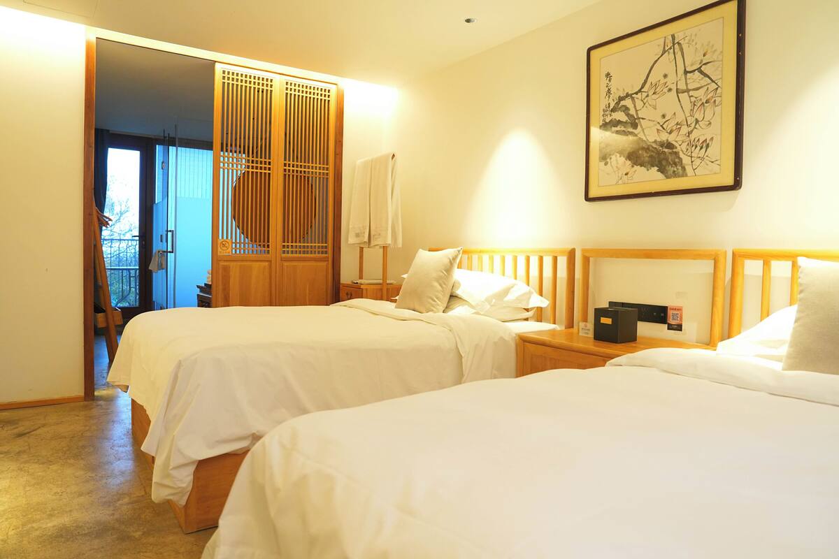 A hotel room with two beds, a wooden headboard, a wall-mounted artwork, and a sliding door leading to a balcony.