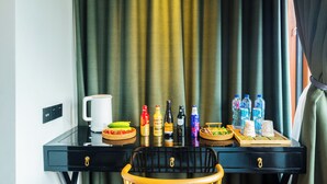 Habitación de hotel con un escritorio negro, una taza blanca, botellas de bebidas y una bandeja con alimentos.