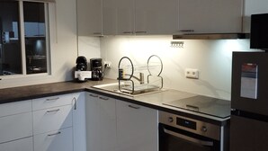 Eine kompakte Küche mit weißen Schränken, einem Edelstahl-Kühlschrank, einem Einbauofen und einer Kaffeemaschine.
