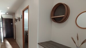 Ein Flur mit Holzboden, einer weißen Wand mit Spiegel und Bilderrahmen und einer Tür zu einem weiteren Raum.