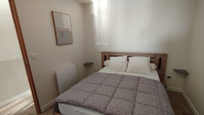 Ein Schlafzimmer mit Bett, Nachttisch, Wandspiegel und Deckenleuchte.