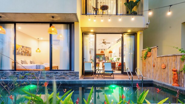 A modern pool area with a glass-enclosed spa room, outdoor seating, and a bamboo fence.