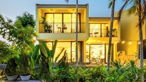 A modern two-story building with balconies, potted plants, and outdoor seating.
