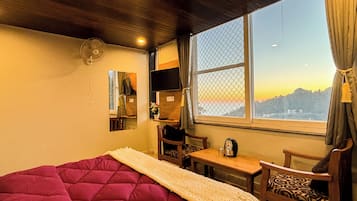 Una habitación con cama, una mesa, una silla, televisor y ventana con vista a las montañas.