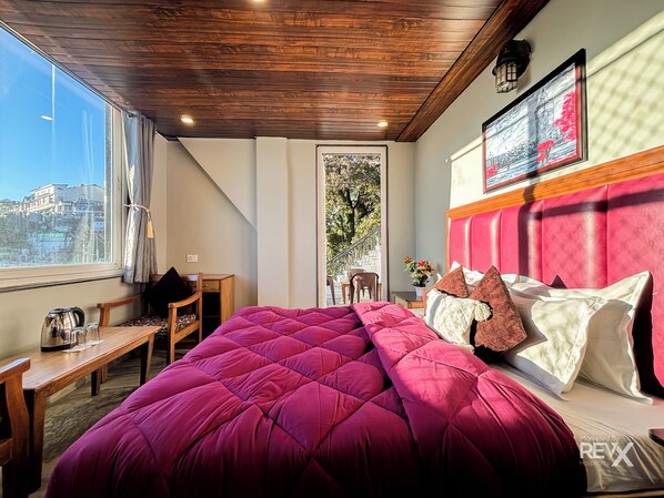 A bedroom with a large bed, wooden furniture, a view of the city, and a red headboard.