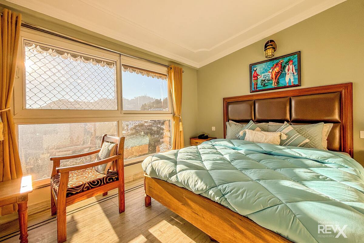 A bedroom with a large bed, a wooden chair, a nightstand, and a painting on the wall.