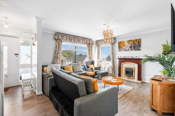 A modern living room with a grey sofa, a fireplace, and a large window with curtains.