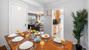 Un coin repas avec une table en bois mise pour le petit-déjeuner, comprenant des assiettes, des verres et un vase avec des fleurs.